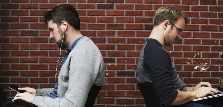Two men working on their computers sitting back to back